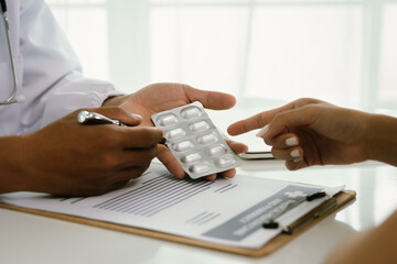 A doctor consults with a patient, explaining medical documents at a desk with a clipboard, laptop,...