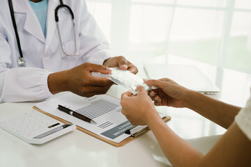 A doctor consults with a patient, explaining medical documents at a desk with a clipboard, laptop,...
