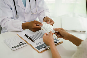 A doctor consults with a patient, explaining medical documents at a desk with a clipboard, laptop,...
