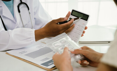 A doctor consults with a patient, explaining medical documents at a desk with a clipboard, laptop, and calculator, emphasizing care, professionalism, and clear communication.