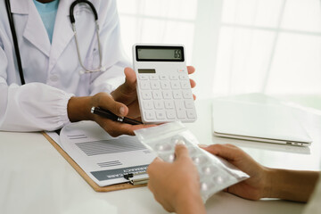 A doctor consults with a patient, explaining medical documents at a desk with a clipboard, laptop,...