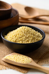 Yellow millet grain in black bowl with scoop, Food ingredient