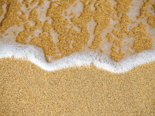 Wave of the sea on a sandy pink beach creating sea foam. Calm ocean water waves splashing sandy beach. Close up sea waves breaking sand beach. Top view, nature background travel relax.