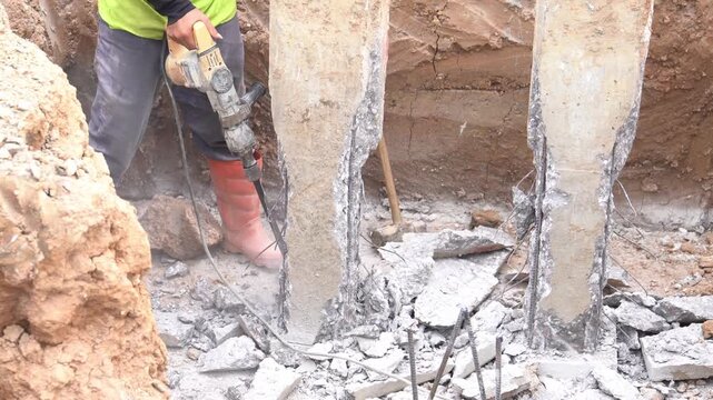 A construction worker is operating a jackhammer to demolish the pile cap for foundation pouring.