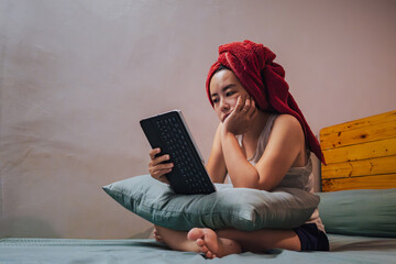 Woman using digital tablet in bed with towel on head