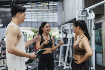 Personal trainer showing thumbs up with two women in a fitness center