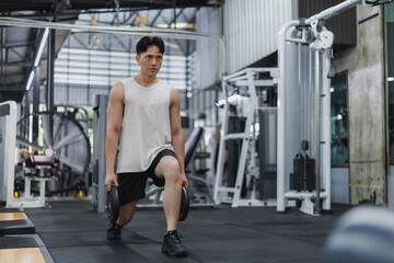 Determined asian athlete performing lunges with weights in modern gym
