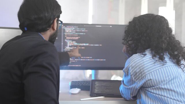 A senior Indian developer mentoring a colleague, pointing at code during a collaborative pair programming session. Concept for teamwork, knowledge transfer, and agile development.