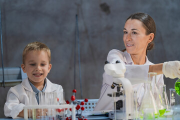 A female teacher or mother explains a molecule model to a curious young boy in a science lab....