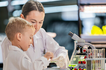 A female teacher or mother explains a molecule model to a curious young boy in a science lab....