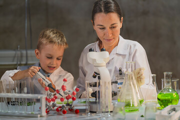 A female teacher or mother explains a molecule model to a curious young boy in a science lab....