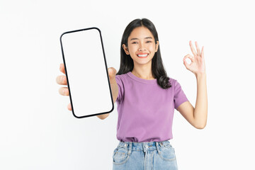 Smiling asian woman holding smartphone with blank screen and shows ok sign on white background