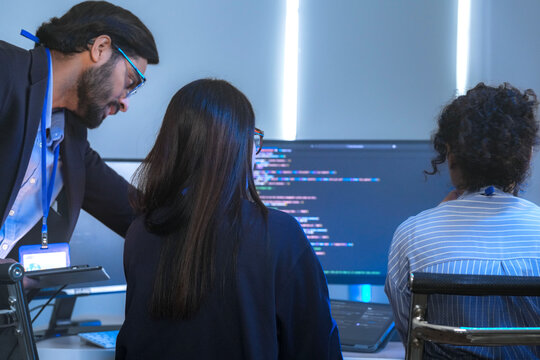 A senior software engineer leads a code review session, mentoring his diverse team on a complex project. Concept for agile development, knowledge transfer, and teamwork.