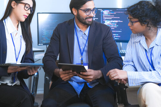 Diverse team of software engineers and data scientists collaborating on a project, using tablets and analyzing code. Concept for AI development, cybersecurity, and tech innovation.