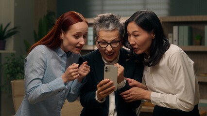 Happy excited women colleagues team group holding mobile phone multinational read good news businesswomen winning online finance celebrating office success offer ladies bet multiracial business people