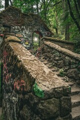 Abandoned stone structure covered in graffiti surrounded by lush greenery