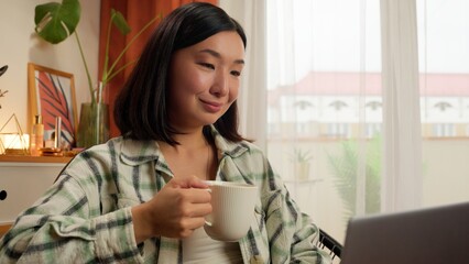 Asian Korean Chinese Japanese woman holding cup drinking coffee female typing laptop girl working computer businesswoman business indoor office lady employee at home freelancer morning work breakfast
