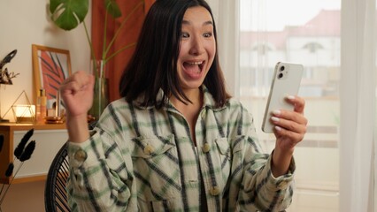 Happy excited Asian Korean lady using mobile phone smartphone reading good news Chinese Japanese...