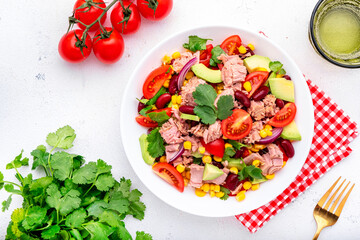 Mexican style salad with canned tuna, avocado, corn, red beans, cherry tomatoes and cilantro, white table background, top view
