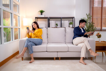 Unhappy asian couple sitting on sofa having relationship problem in living room at home, emotion conflict and disconnect, couple with frustrated and disappointed, ignoring and trouble with expression.