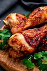 Baked chicken legs or drumsticks in hot chili paprika pepper marinade on wooden serving board, black background, top view