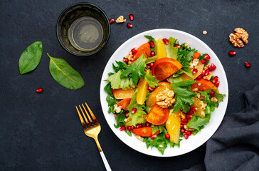 Autumn vegan persimmon salad with pomegranate seeds, walnuts, orange slices and lettuce, black...