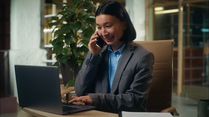 Cheerful Asian Korean Chinese Japanese woman smiling talking mobile phone smartphone with client consultation call female businesswoman work laptop business girl office manager employee entrepreneur