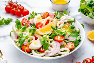 Gourmet seafood salad with squid, juicy orange, red tomatoes, lamb lettuce on marble table, top view