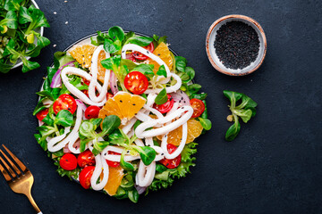 squid salad with oranges, tomatoes, lettuce and lemon dressing, black background, top view