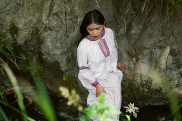 Indigenous woman wearing traditional clothes relaxing by a stream in the rainforest