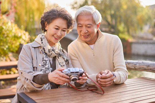 Senior couple seated at a sidewalk caf��, looking through the photos they just snapped
