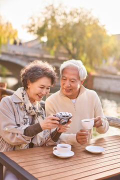 Senior couple seated at a sidewalk caf��, looking through the photos they just snapped
