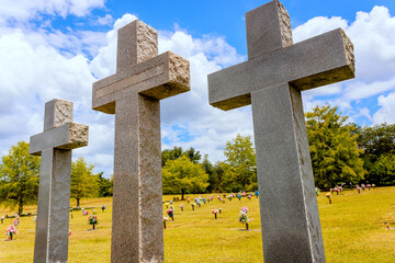 Three tall crosses stand in peaceful cemetery surrounded by greenery flower arrangements.