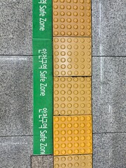 Green line that marks the safety zone line in metro station in Seoul. Yellow tactile paving or...