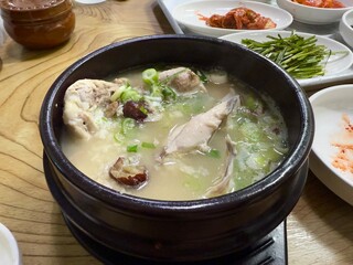 Samgyetang served hot in ttukbaegi or the black hot pot with various side dish on the table in a restaurant