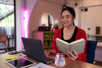 Asian adult woman freelancer digital nomad productive works laptop reads book developing skills at...
