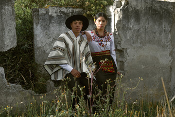 Indigenous couple posing by a concrete wall in traditional clothing