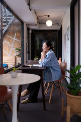 Asian young adult woman freelancer nomad enjoying a relaxed moment at a modern vibrant coworking space cafe with beautiful window view