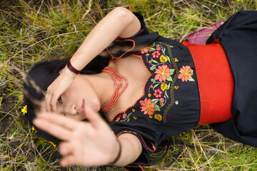 Indigenous model wearing traditional dress lying in grass covering her face