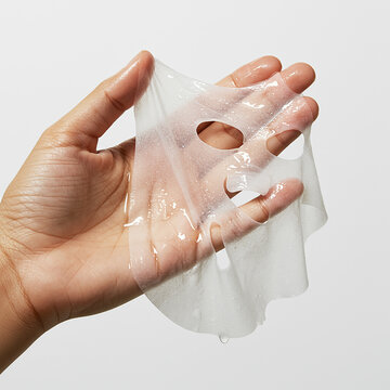 A hand holds a wet sheet mask, ready for skincare