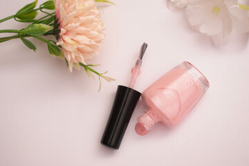 Close-up of a pink nail polish bottle with the cap off, next to delicate artificial flowers on a...