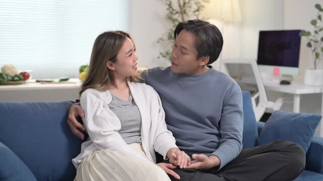 man and woman are sitting on a blue couch, holding hands. The woman is wearing a white shirt and the man is wearing a blue shirt. Scene is warm and affectionate