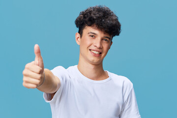 smiling man showing thumbs up gesture with friendly expression, casual white t-shirt, curly hair,...
