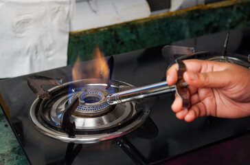 A women's hand lights the gas on a kitchen stove. A cook lights a gas stove to cook food.