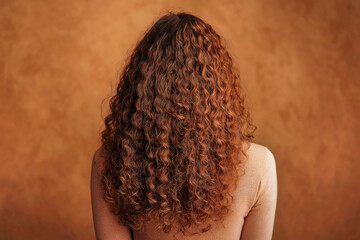 Young woman with natural wavy loose hair on brown background close-up view from behind.