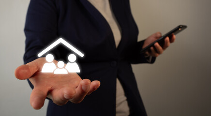Businesswoman holding a cell phone while holding a virtual icon of a family in her other hand.
