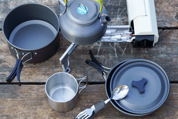 Metal camping cookware set with kettle on portable gas stove placed on wooden table, ready for...