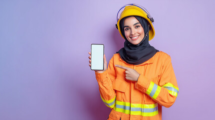 Smiling Muslim female firefighter wearing hijab, pointing at a smartphone with a blank screen. Ideal for app mockups, emergency services, diversity, and tech promotion concepts.