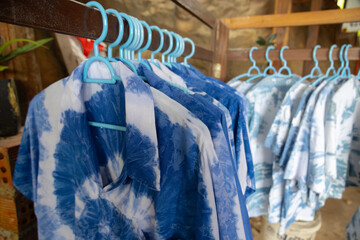 close-up shot of tie-dye t-shirts hanging on light blue plastic hangers. The shirts feature a soft, pastel tie-dye pattern.