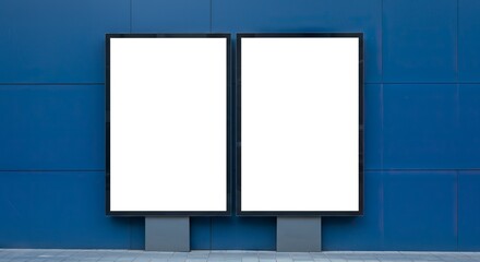 Two blank blackframed billboards stand on a gray walkway against a blue panel wall